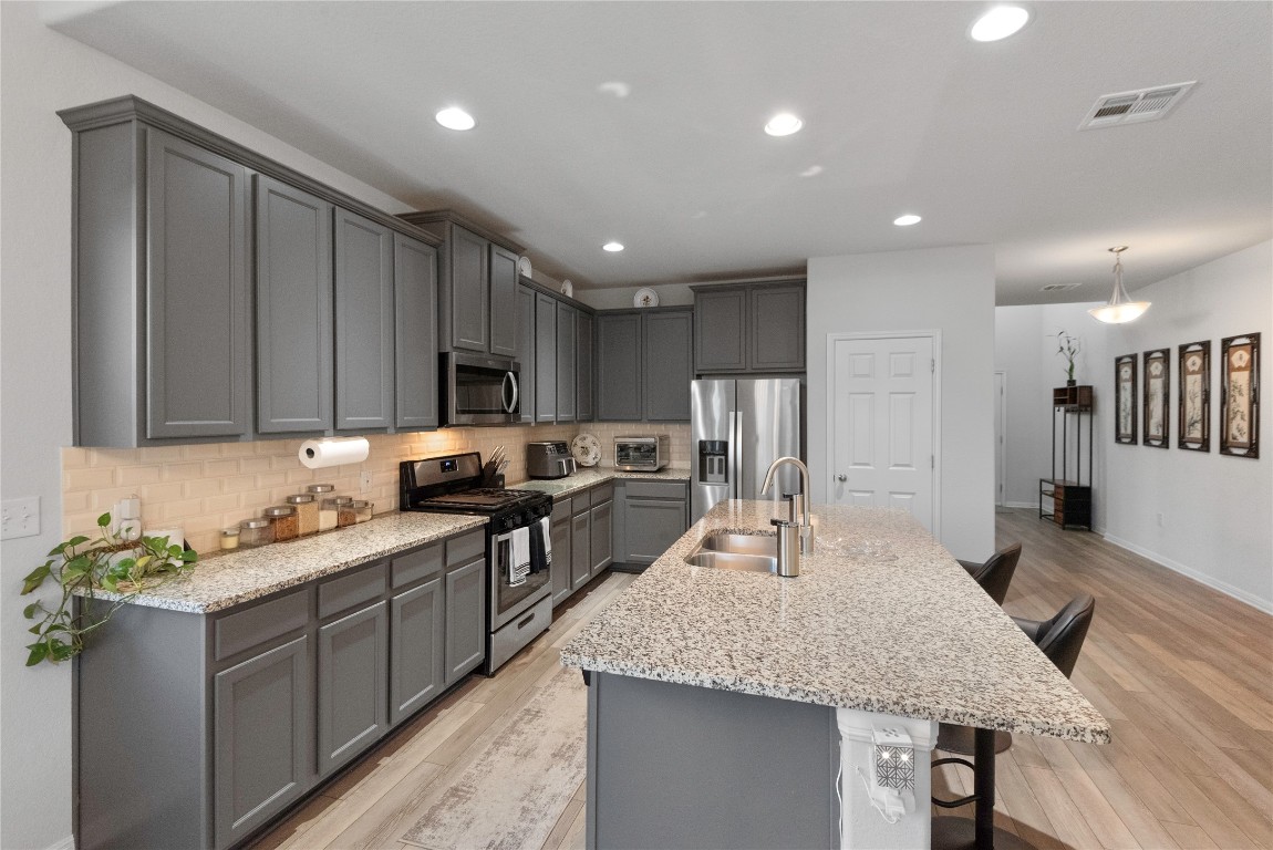 932 Medina Way Leander, TX 78641 - Photo 8 of 28 Kitchen with gray cabinets, a kitchen bar, stainless steel appliances, tasteful backsplash, and light stone countertops