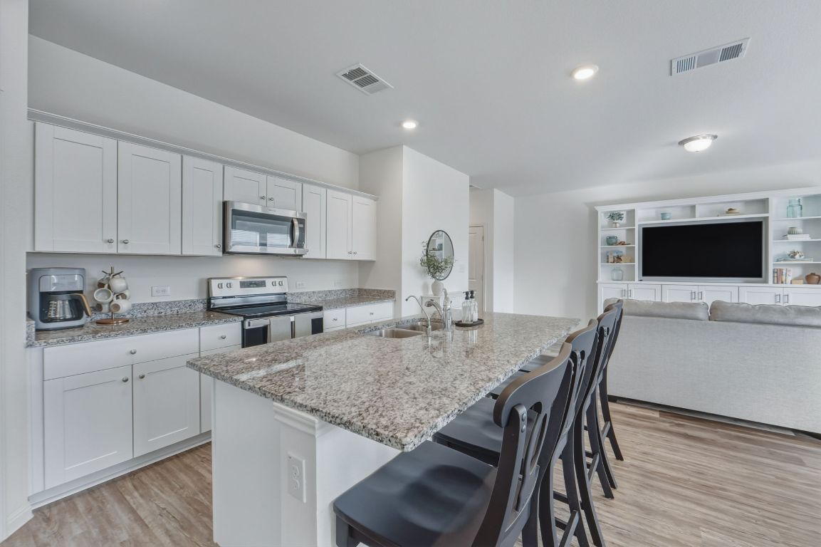 201 Wonderful Life Way Jarrell, TX 76537 - Photo 39 of 39 Kitchen with a kitchen breakfast bar, stainless steel appliances, light stone counters, open floor plan, and light wood-style floors