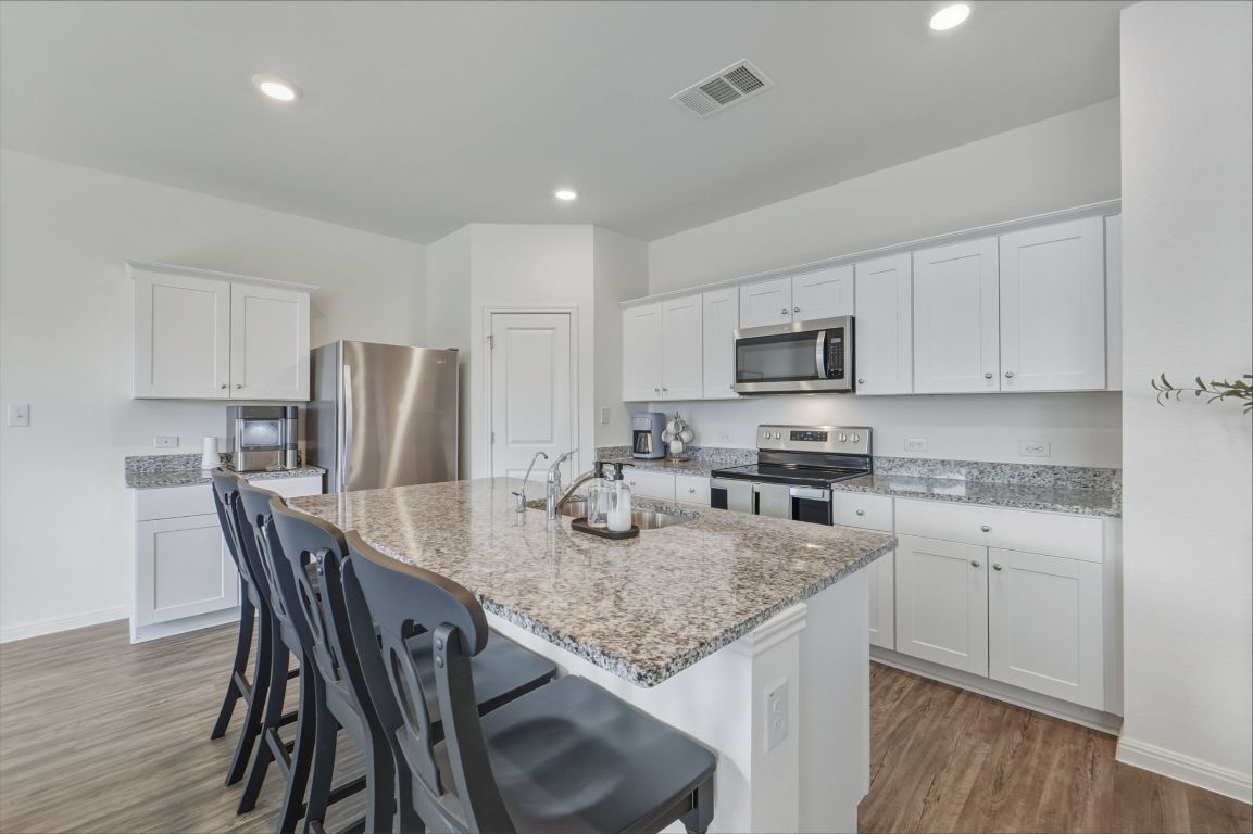 201 Wonderful Life Way Jarrell, TX 76537 - Photo 10 of 39 Kitchen featuring a breakfast bar, appliances with stainless steel finishes, white cabinets, light wood finished floors, and recessed lighting