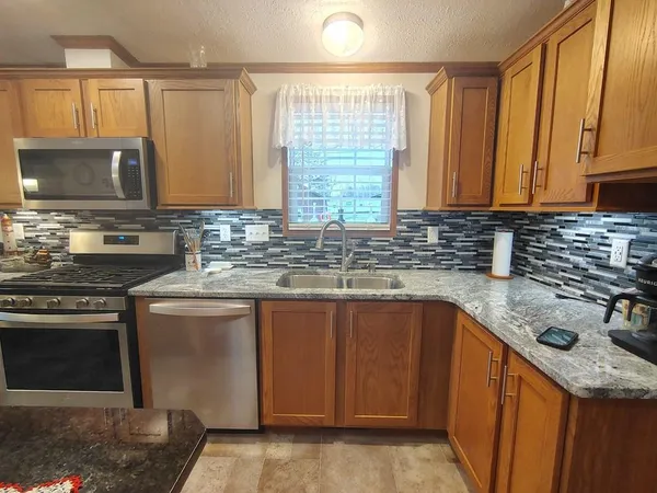 a kitchen with stainless steel appliances granite countertop a refrigerator a stove top oven a sink dishwasher and wooden cabinets with wooden floor