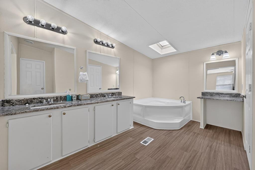 13405 Wheat Road Venus, TX 76084 - Photo 26 of 32 Bathroom featuring wood-finish flooring, a corner soaking tub, a skylight, a double vanity with granite-style countertops, and a separate vanity area