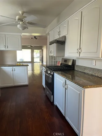 a kitchen with granite countertop a stove a sink dishwasher and white cabinets with wooden floor