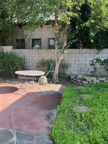 a view of a backyard with table and chairs potted plants and large tree