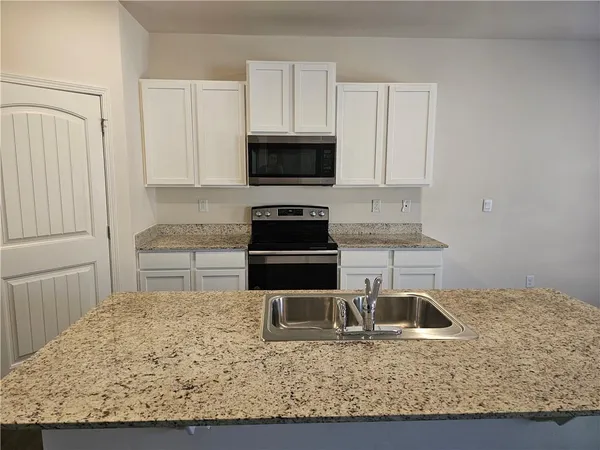 a kitchen with granite countertop a stove a sink and a white cabinets