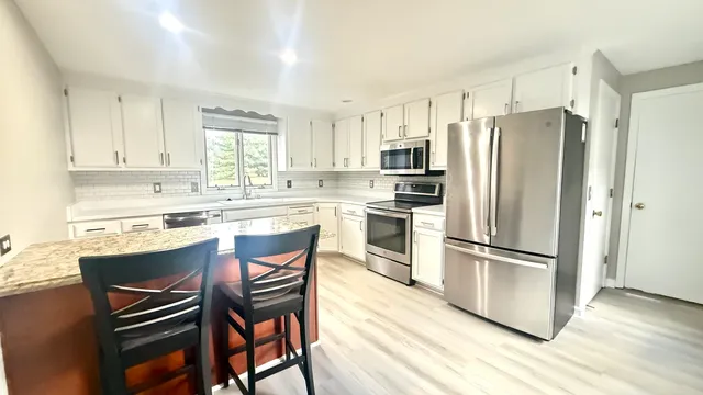 a kitchen with stainless steel appliances a refrigerator a stove a sink and white cabinets with wooden floor