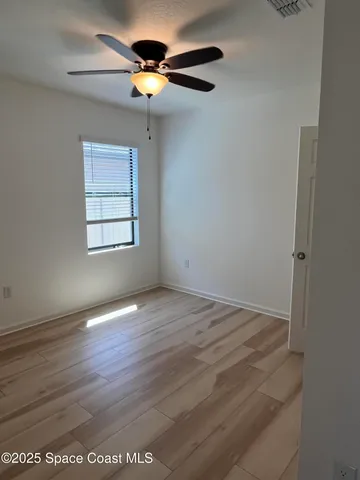 an empty room with wooden floor chandelier fan and windows