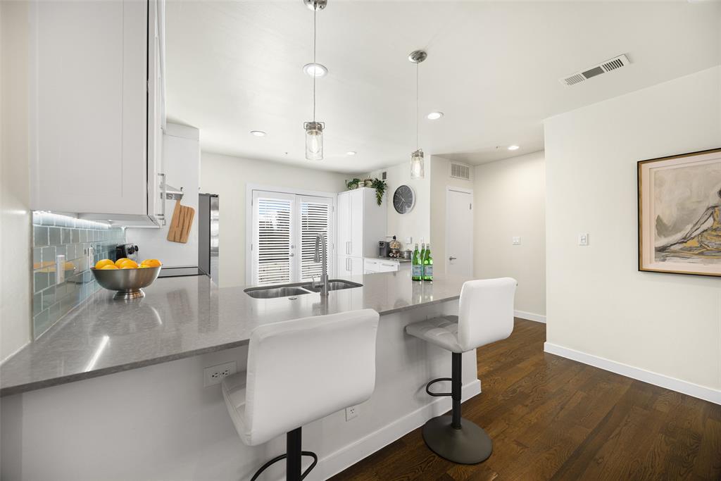 3922 Gilbert Avenue, Unit 214 Dallas, TX 75219 - Photo 4 of 27 Modern kitchen featuring white cabinetry, a large kitchen island with a double basin sink, and pendant lighting