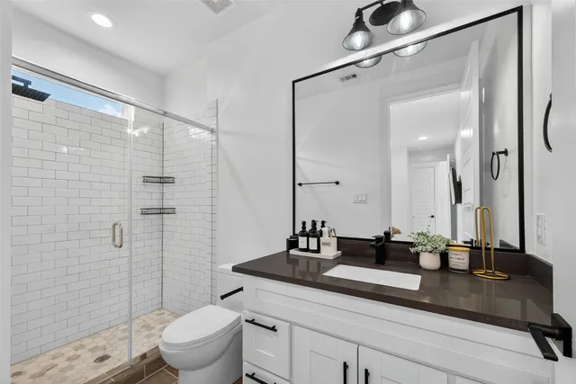 a bathroom with a granite countertop sink a toilet a mirror and shower