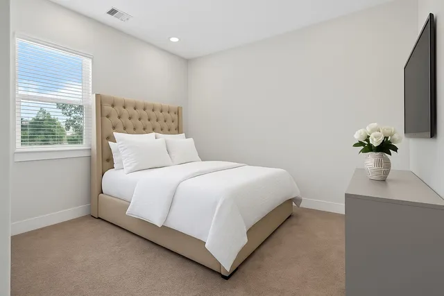 a bedroom with a bed potted plant on dresser and a window