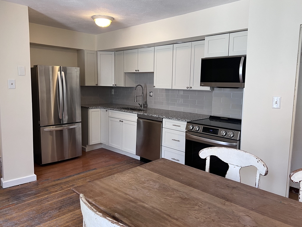 394 Broadway, Unit 3 Somerville, MA 02145 - Photo 3 of 12 a kitchen with stainless steel appliances kitchen island granite countertop a stove a refrigerator and a microwave