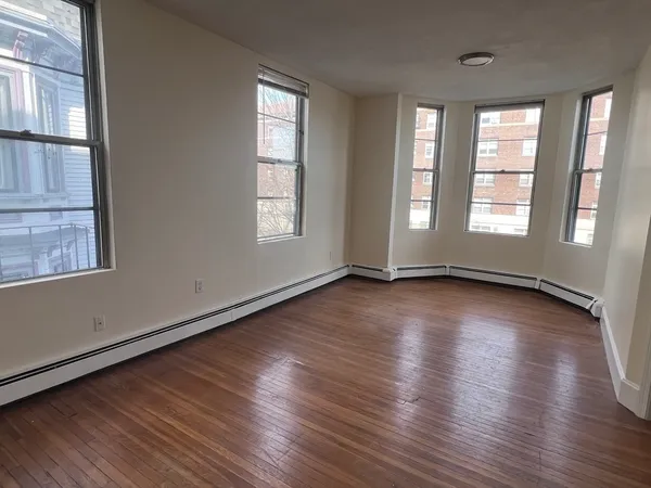 an empty room with wooden floor and windows with curtains