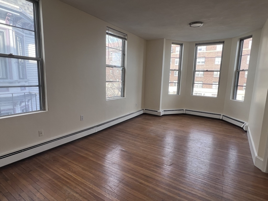 394 Broadway, Unit 3 Somerville, MA 02145 - Photo 6 of 12 an empty room with wooden floor and windows with curtains