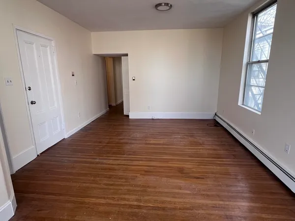a view of an empty room with wooden floor and a window