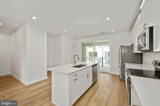 a kitchen with granite countertop a stove top oven a sink a refrigerator and white cabinets with wooden floor