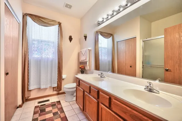 a spacious bathroom with a double vanity sink a toilet a mirror and shower