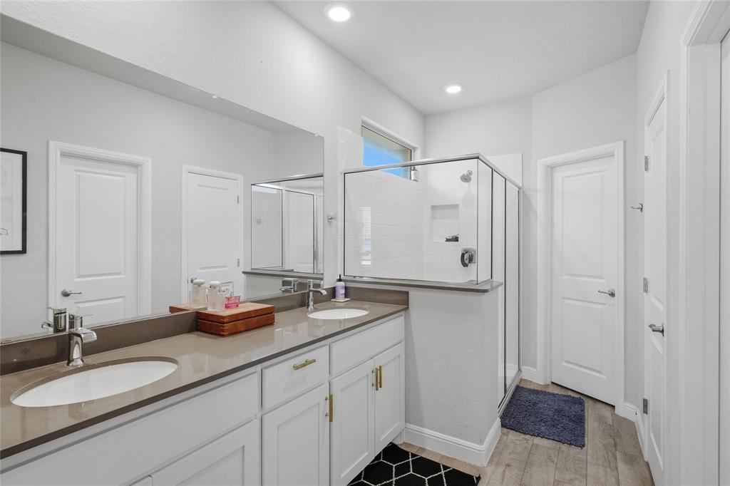 1812 Ruffian Road Granbury, TX 76049 - Photo 29 of 37 Dual vanity with undermount sinks and extensive countertop space, glass-enclosed shower with subway tile surround, white cabinetry with gold-tone hardware, and wood-finish flooring
