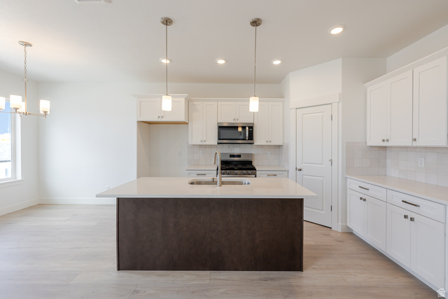 4748 Heartwood Road, Unit 434 Mapleton, UT 84664 - Photo 11 of 18 Dual tone kitchen with light wood-style flooring, a center island with sink, stainless steel appliances, light stone counters, and a chandelier