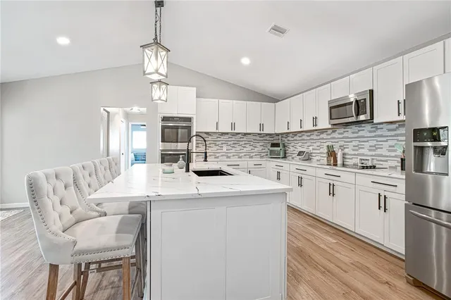 a kitchen with stainless steel appliances kitchen island granite countertop a sink a stove a refrigerator cabinets a dining table and chairs