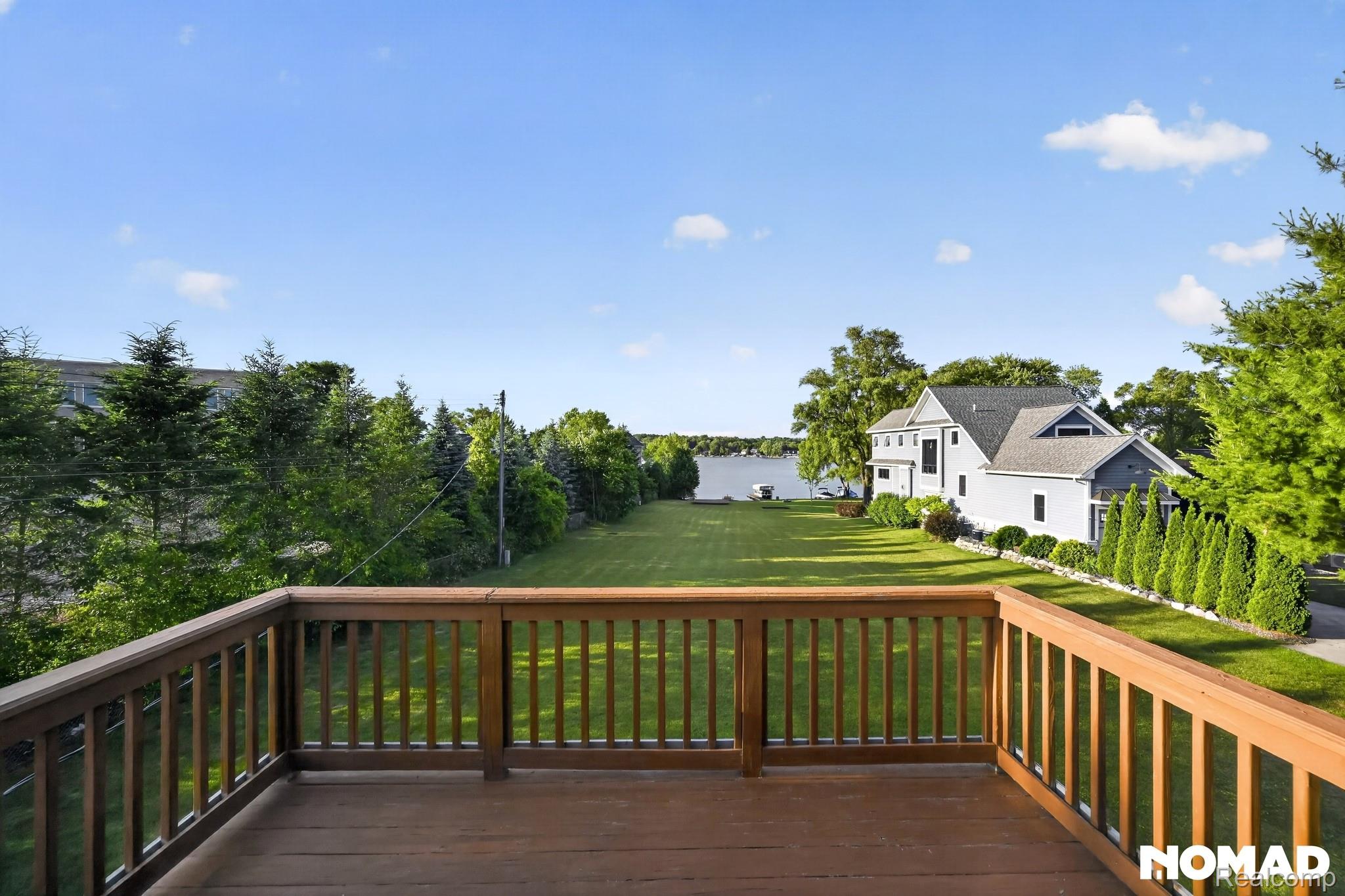 8315 Hilton Road Brighton, MI 48114 - Photo 5 of 26 Spacious outdoor deck with wood railing, overlooking a substantial lawn leading to a body of water