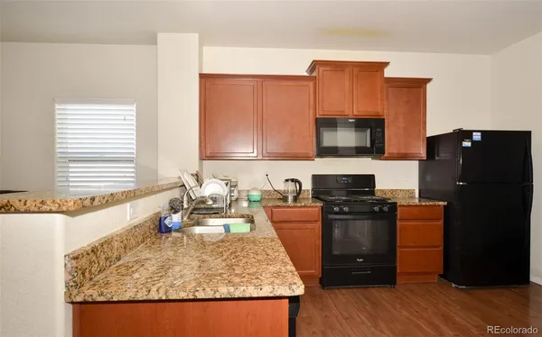 a kitchen with granite countertop wooden cabinets a stove top oven a refrigerator and dishwasher with wooden floor