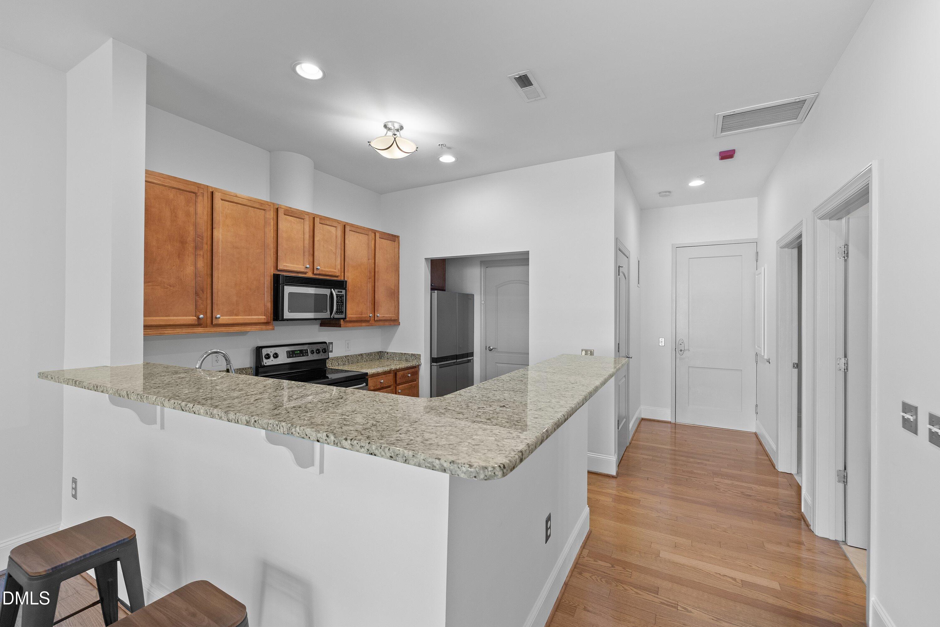 317 West Morgan Street, Unit 215 Raleigh, NC 27601 - Photo 5 of 38 a large kitchen with kitchen island granite countertop a sink and dishwasher a oven with wooden cabinets