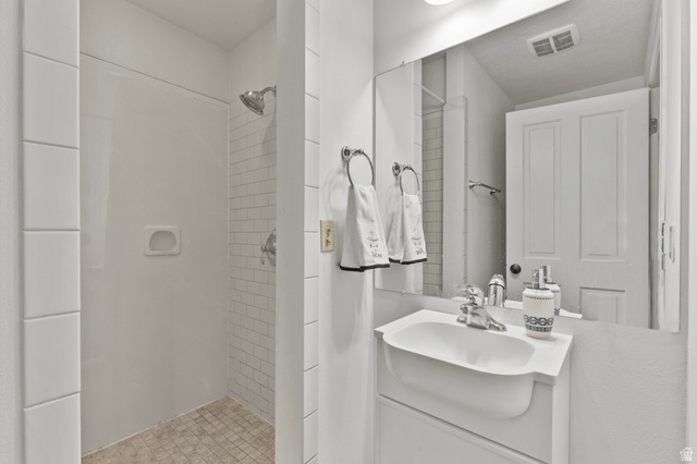 148 South 300 East Logan, UT 84321 - Photo 13 of 29 White bathroom featuring a single vanity with a ceramic sink, a large wall-mounted mirror, and a tiled shower with subway tile accents and a chrome showerhead