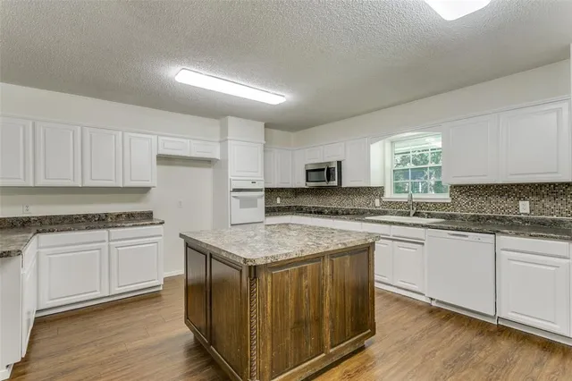 a kitchen with stainless steel appliances granite countertop a stove top oven a sink dishwasher and white cabinets with wooden floor