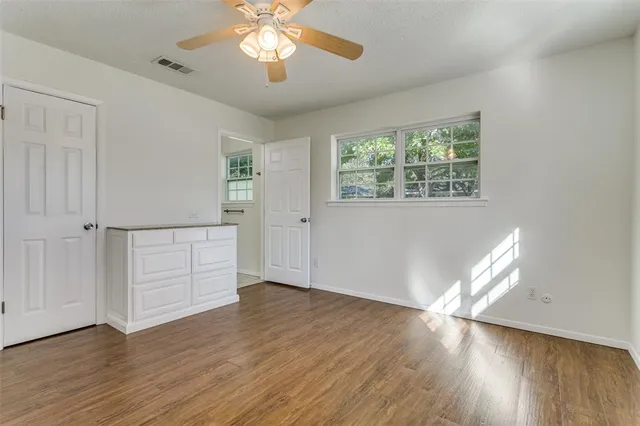 an empty room with wooden floor chandelier fan and windows