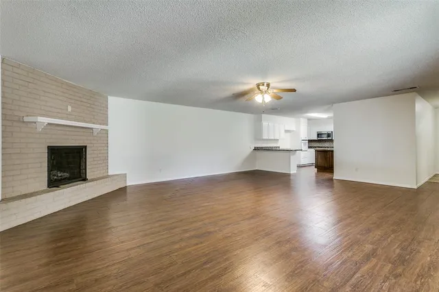 a view of an empty room with kitchen and fireplace