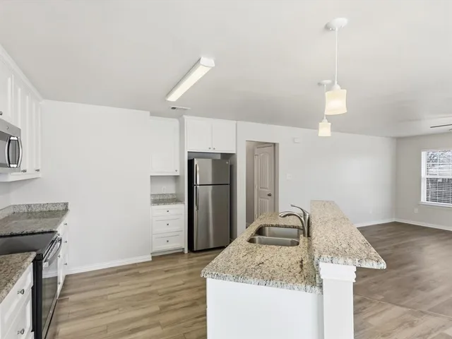 a kitchen with granite countertop a refrigerator a sink a stove and wooden floor