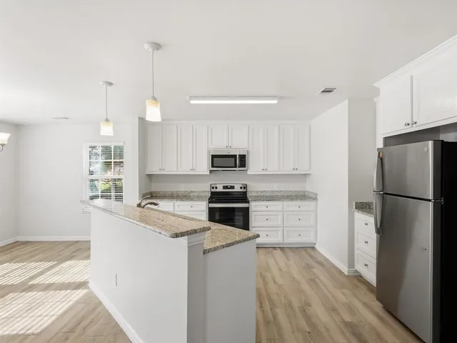 a kitchen with a refrigerator stove and white cabinets with wooden floor