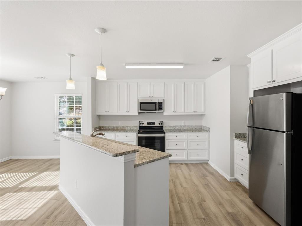 6409 Ramey Avenue Fort Worth, TX 76112 - Photo 17 of 25 a kitchen with a refrigerator stove and white cabinets with wooden floor