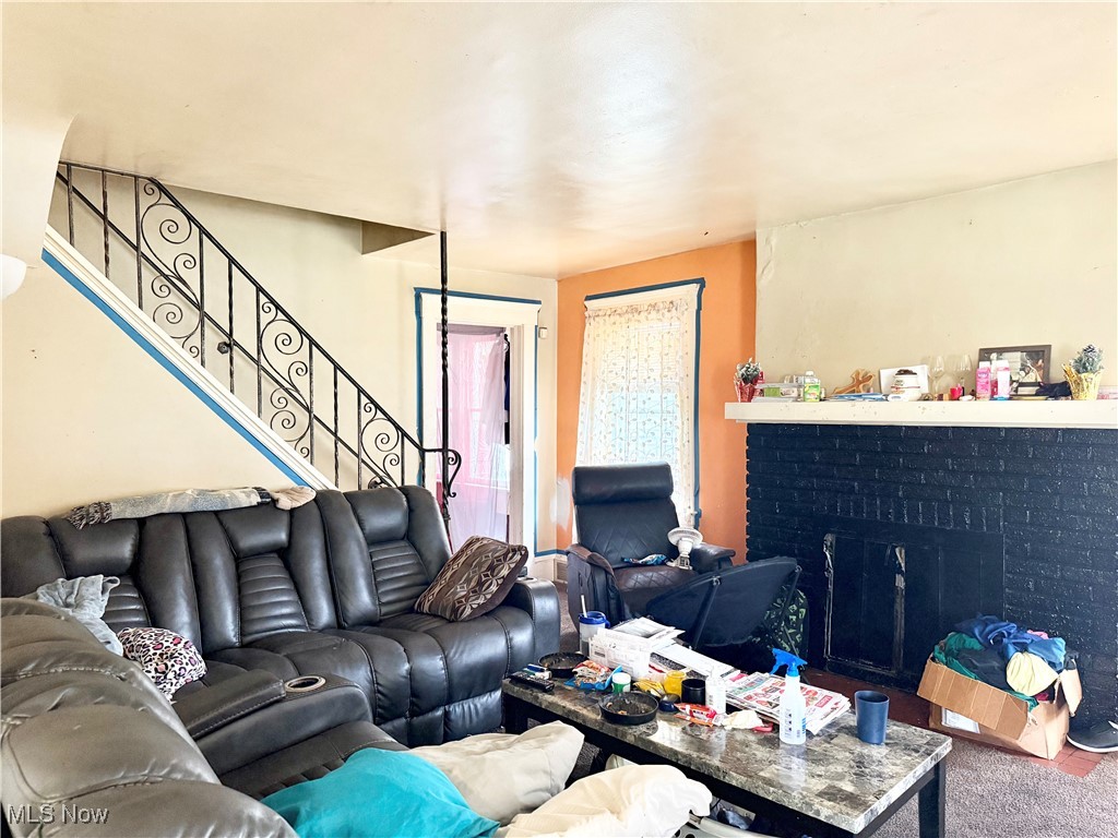 Living area featuring a brick fireplace, stairway, and carpet flooring