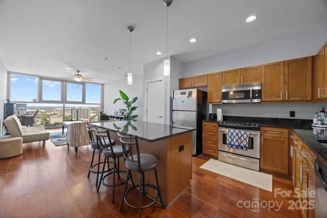 a kitchen with stainless steel appliances granite countertop a refrigerator a stove a sink a dining table and chairs with wooden floor