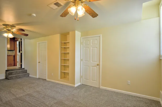 an empty room with a chandelier fan and wooden floor