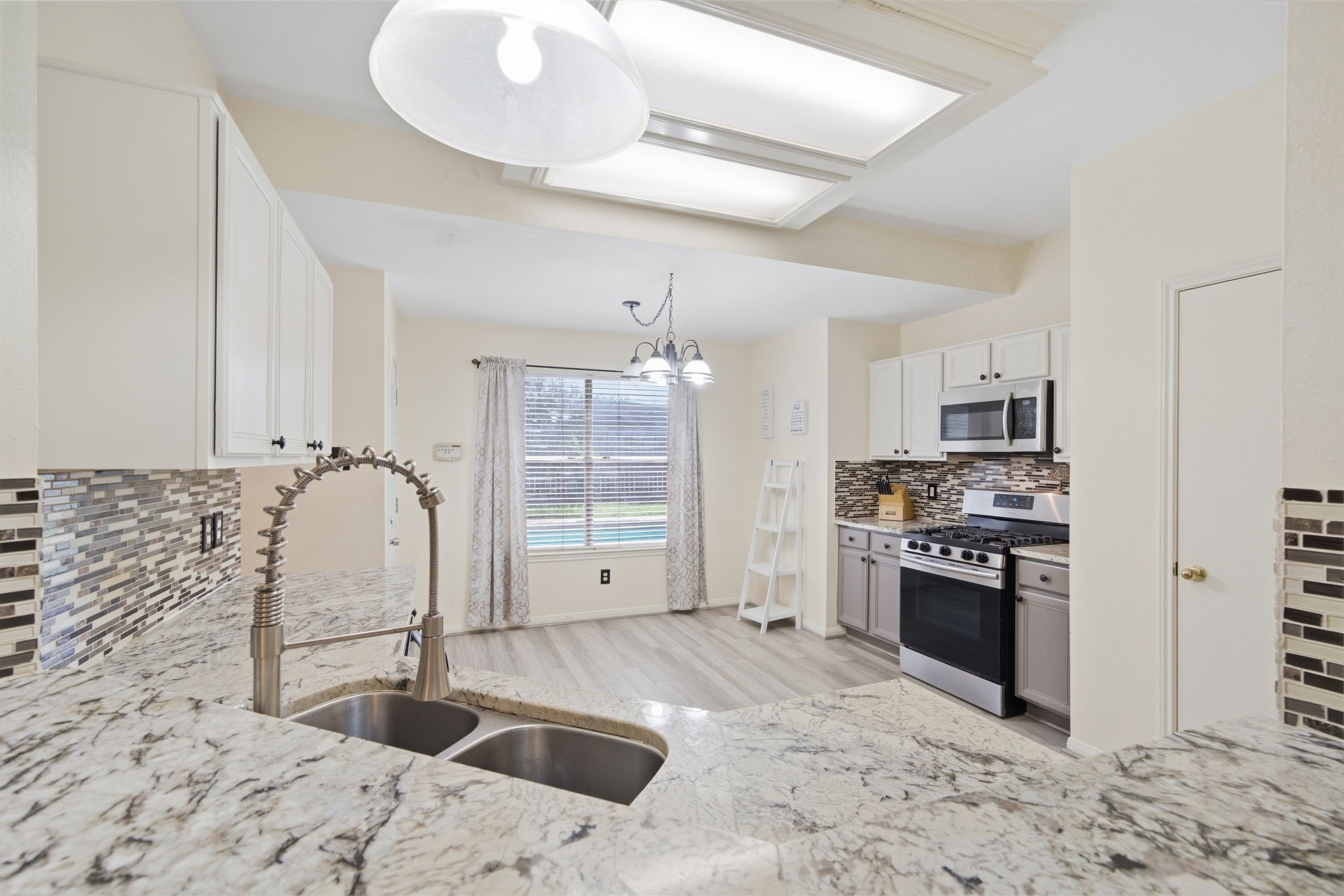 6911 River Road Richmond, TX 77469 - Photo 18 of 36 Granite countertops and an undermount dual sink create a functional workspace, with an open peninsula overlooking the breakfast area. A wide window brings natural light across low-maintenance flooring, while sleek appliances and a nearby pantry door add everyday convenience.
