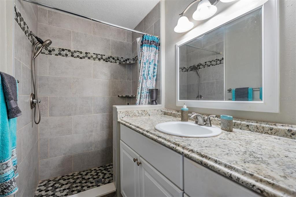 11308 Versailles Lane, Unit C Port Richey, FL 34668 - Photo 18 of 33 a bathroom with a granite countertop sink a mirror a vanity and shower
