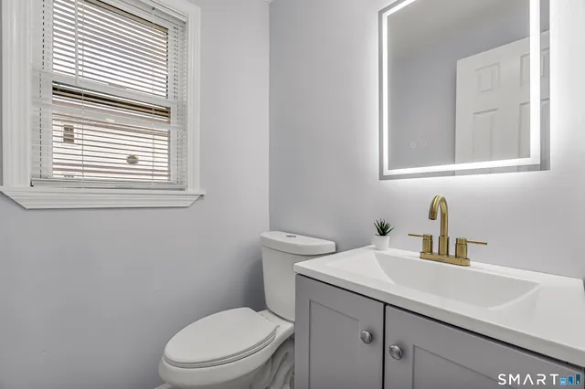 a bathroom with a toilet a sink a mirror and a window