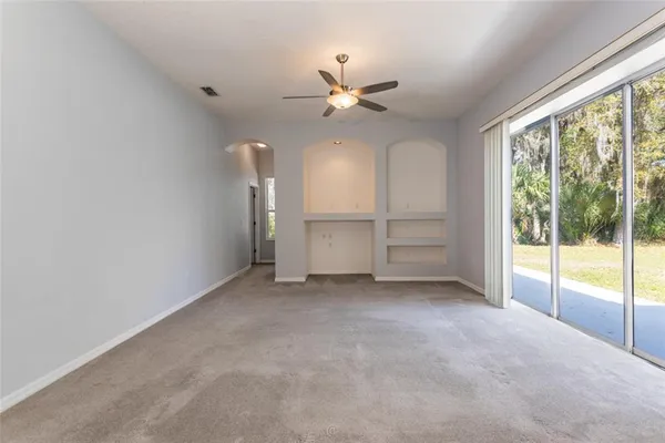 an empty room with chandelier fan and windows