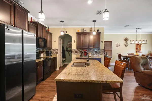 a kitchen with stainless steel appliances kitchen island granite countertop a refrigerator a oven a sink with island and chairs