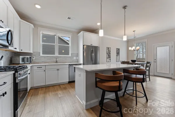 a kitchen with stainless steel appliances granite countertop a stove a sink dishwasher a refrigerator and a dining table with wooden floor