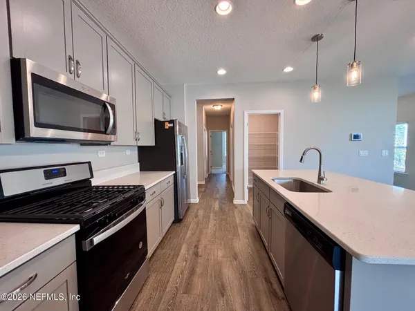 a kitchen with granite countertop a stove top oven a sink dishwasher a refrigerator and white cabinets with wooden floor