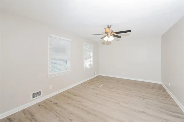an empty room with wooden floor fan and windows