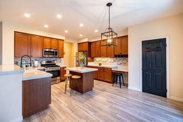 a kitchen with stainless steel appliances granite countertop a refrigerator a stove top oven a sink dishwasher and a dining table with wooden floor