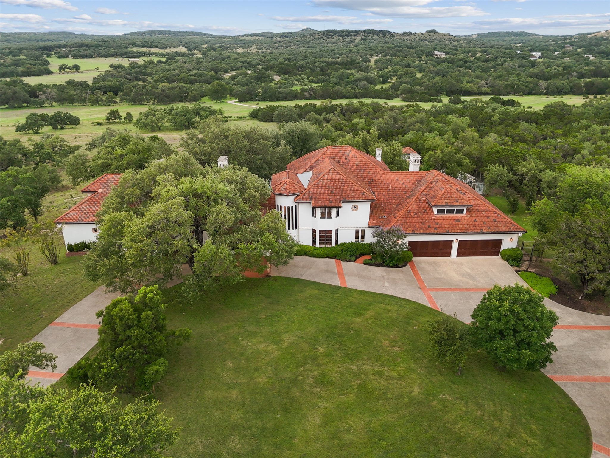 34000 Smithson Valley Road Bulverde, TX 78163 - Photo 48 of 50 A breathtaking aerial perspective showcases the estate’s authentic Mediterranean architecture, sweeping circular drive, and serene setting among mature Texas live oaks. Rolling Hill Country vistas stretch for miles beyond the property.