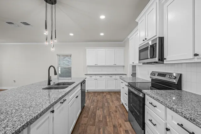 a kitchen with granite countertop a sink stainless steel appliances and white cabinets