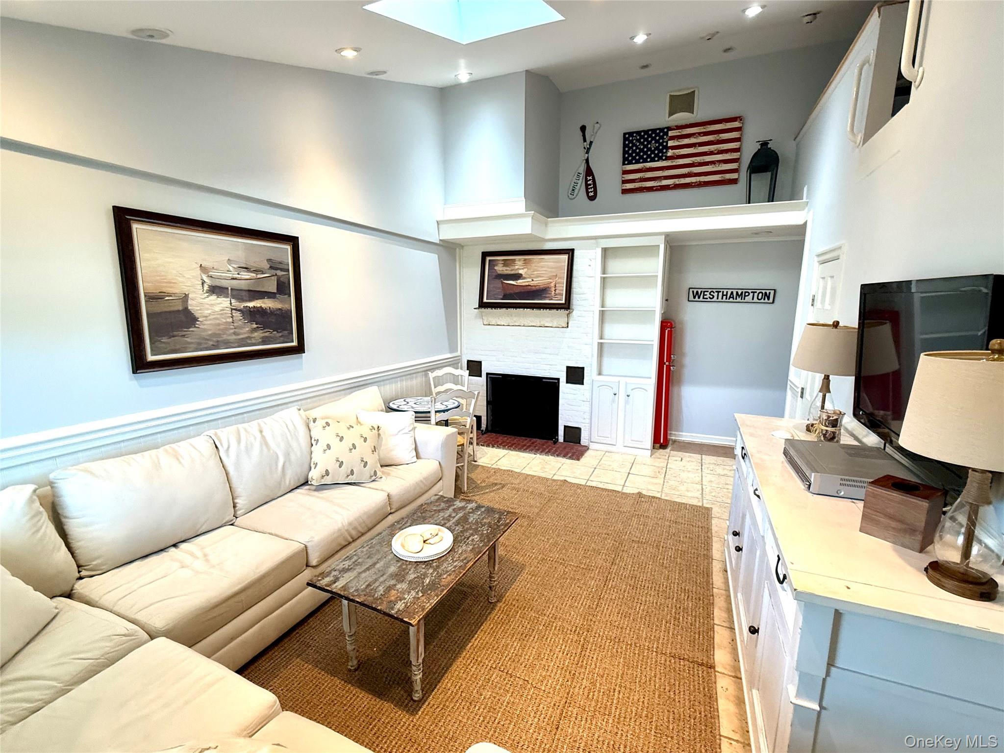 231 Dune Road, Unit 905 Westhampton Beach, NY 11978 - Photo 1 of 24 Living area with a skylight, recessed lighting, a fireplace with raised hearth, a high ceiling, and light tile patterned floors