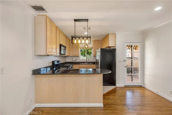 a kitchen with stainless steel appliances granite countertop a refrigerator a sink dishwasher a stove and a dining table with wooden floor