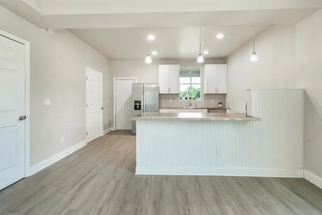 a kitchen with kitchen island a sink a stove a refrigerator and white cabinets with wooden floor