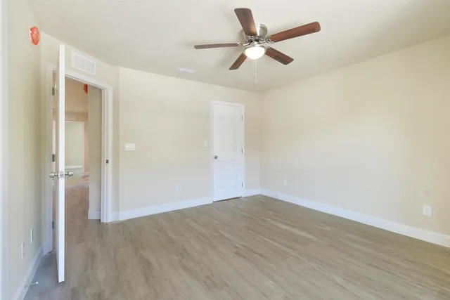an empty room with wooden floor fan and windows